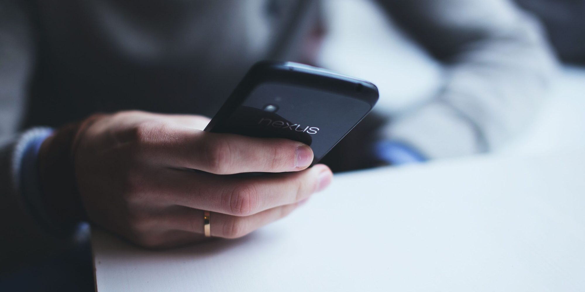 Close-up of a person holding a smartphone while sitting at a white table.